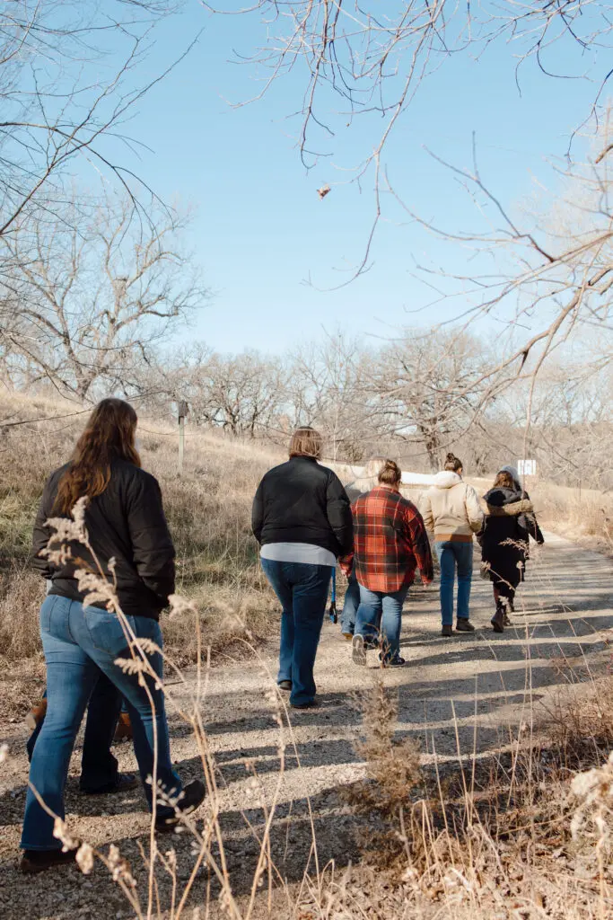 Five women walk in a line on a gravel path outdoors on a nature walk.